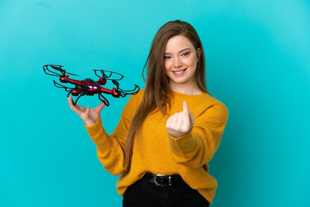 Teenager-Mädchen, das eine Drohne über isoliertem blauem Hintergrund hält und kommende Geste macht