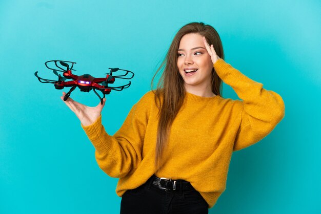 Teenager-Mädchen, das eine Drohne über isoliertem blauem Hintergrund hält und viel lächelt