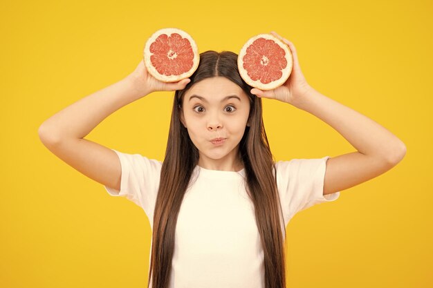 Teenager-Mädchen, das eine Grapefruit auf gelbem Hintergrund hält Lustiges Gesicht