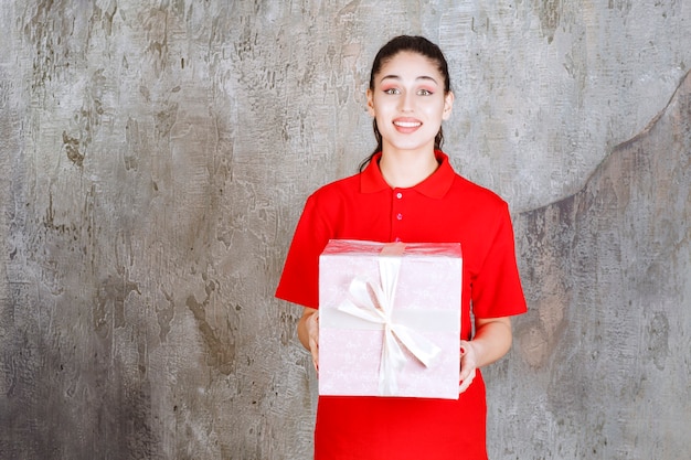 Teenager-Mädchen, das eine rosa Geschenkbox hält, die mit weißem Band umwickelt ist.