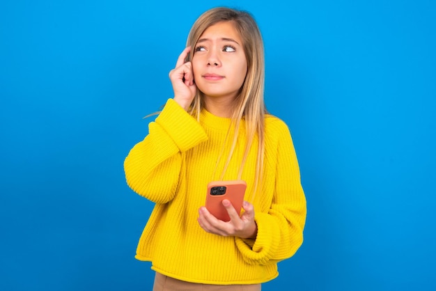 Teenager-Mädchen, das einen gelben Pullover trägt, der ein Gadget hält, während es die Zunge herausstreckt