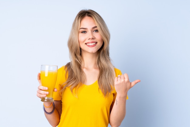 Teenager-Mädchen, das einen Orangensaft lokalisiert auf Blau zeigt zur Seite zeigt, um ein Produkt zu präsentieren