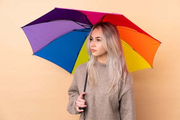 Teenager-Mädchen, das einen Regenschirm über der Wand hält, die Seite schaut