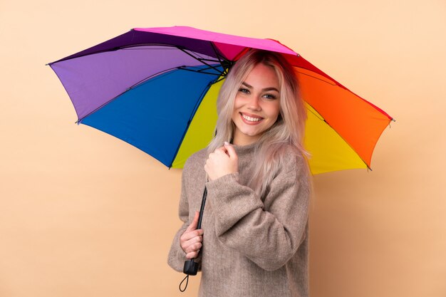 Teenager-Mädchen, das einen Regenschirm über isolierter Wand hält, die einen Sieg feiert