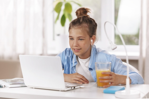 Teenager-Mädchen, das Kopfhörer trägt, die am Tisch sitzen und Hausaufgaben machen