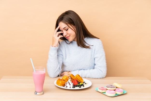 Teenager-Mädchen, das Waffeln auf beige Wand lachend isst