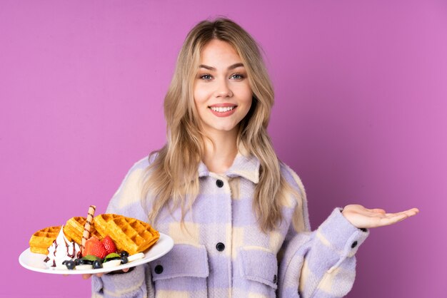 Teenager-Mädchen, das Waffeln lokalisiert auf lila Wand hält