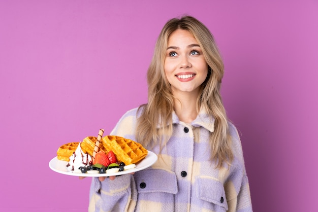 Teenager-Mädchen, das Waffeln lokalisiert hält, die auf lila schauen, während sie lächeln