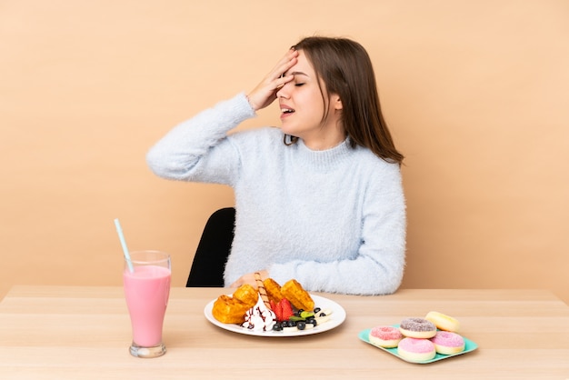 Teenager Mädchen essen Waffeln isoliert auf beige Wand viel lächelnd