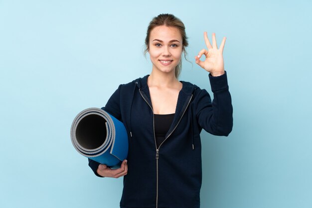 Teenager Mädchen hält Matte auf Blau zeigt ok Zeichen mit den Fingern