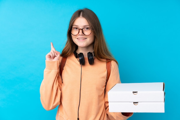 Teenager-Mädchen halten Pizzen über isolierte blaue Wand zeigt eine großartige Idee