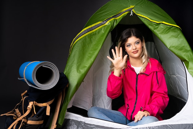 Teenager-Mädchen in einem grünen Zelt des Campings auf schwarzer Wand, die fünf mit den Fingern zählt
