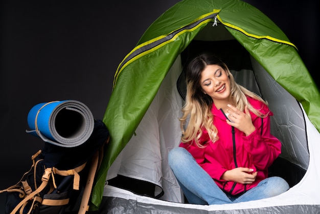 Teenager-Mädchen in einem grünen Zelt des Campings lokalisiert auf schwarzer Wand, die viel lächelt