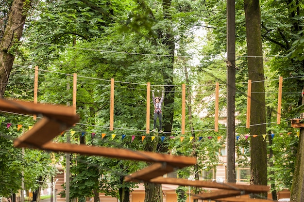 Teenager-Mädchen in einem Helm und Sicherheitsausrüstung im Abenteuerseilpark auf dem Hintergrund der Natur