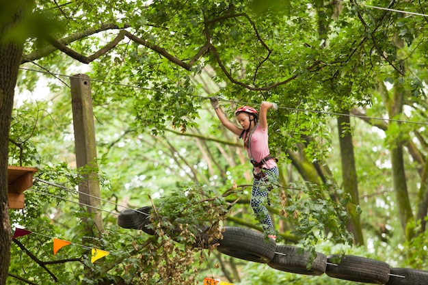 Teenager-Mädchen in einem Helm und Sicherheitsausrüstung im Abenteuerseilpark auf dem Hintergrund der Natur