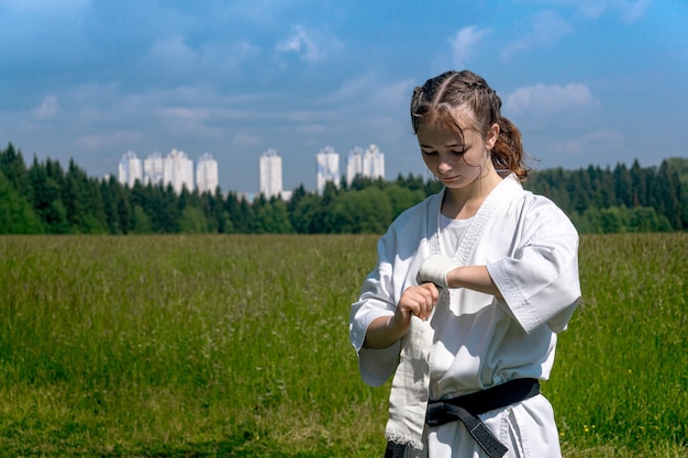 Teenager-Mädchen in einem Kimono, das eine Handgelenkspackung einwickelt, bevor es mit dem Karate-Training im Freien beginnt