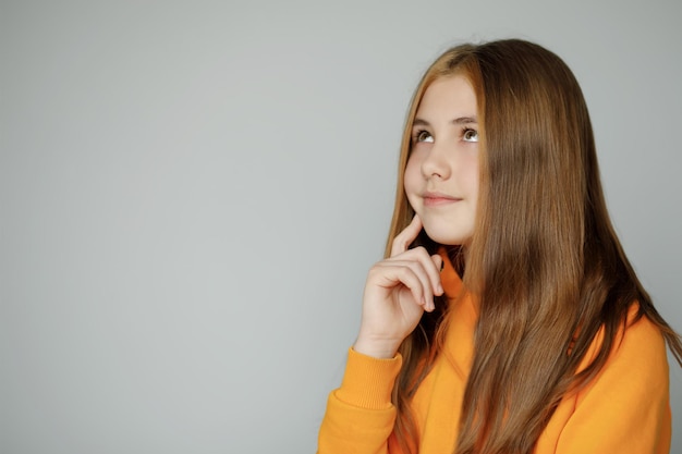 Teenager-Mädchen in einem orangefarbenen Pullover auf grauem Hintergrund träumend zur Seite schauen