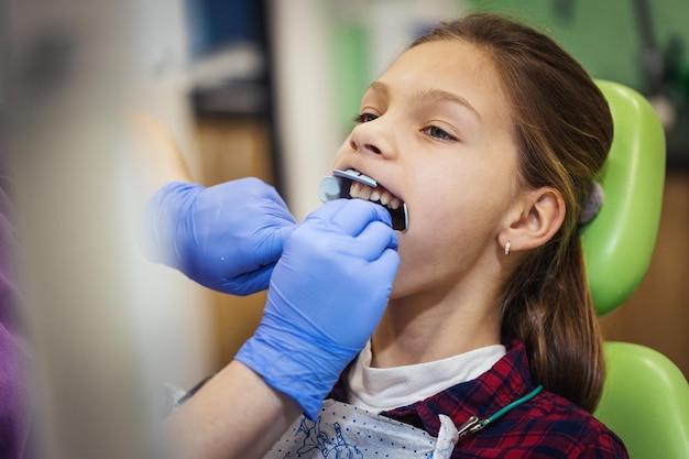 Teenager-Mädchen ist beim Zahnarzt. Sie sitzt auf dem Zahnarztstuhl und der Zahnarzt setzt Zahnspangen auf ihre Zähne.