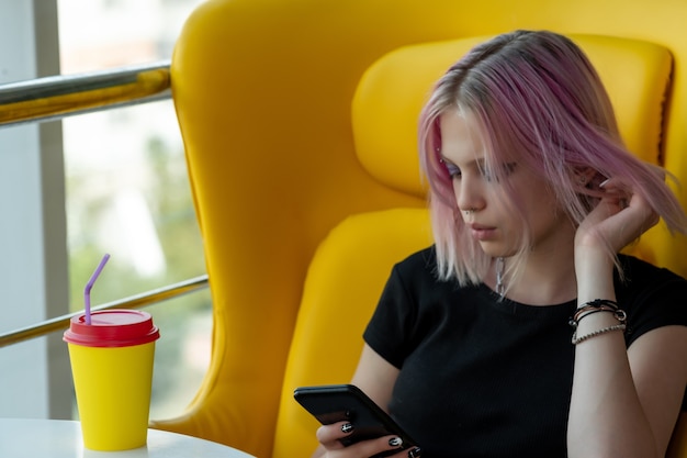 Teenager-Mädchen kommuniziert über das Netzwerk mit dem Telefon, während sie in einem Café sitzt