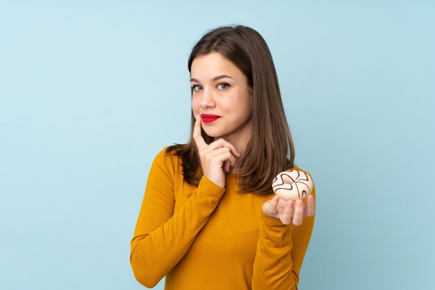 Teenager-Mädchen lokalisiert auf blauer Wand, die einen Donut hält