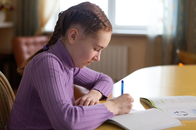 Teenager-Mädchen macht Hausaufgaben Sie sitzt zu Hause am Tisch und schreibt in ein Schulheft