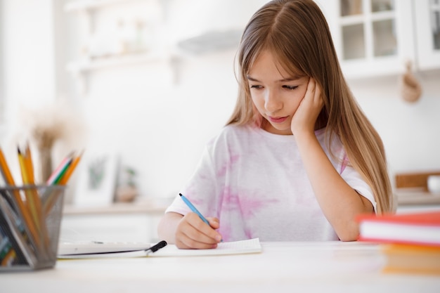 Teenager-Mädchen macht Notizen im Notizblock und macht Hausaufgaben am Tisch zu Hause