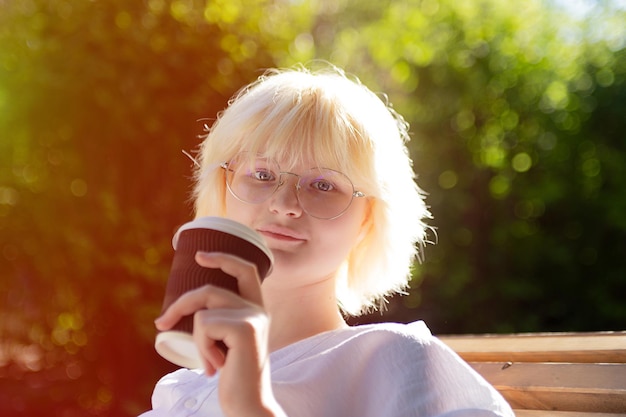 Teenager-Mädchen mit blonden Hören Kaffeetrinken aus Craft Pappbecher Outsidesunlight auf Hintergrund