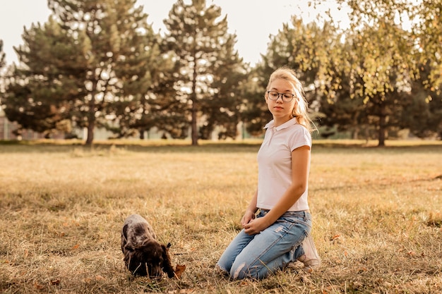 Teenager-Mädchen mit Brille, die auf Gras mit ihrem kleinen Hund spielt