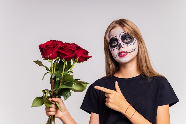 Teenager-Mädchen mit coolem Totenkopf-Make-up mit Rosen auf dem Kopf, das im Studio in die Kamera blickt