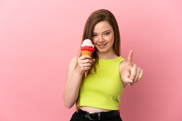 Teenager-Mädchen mit einem Kornett-Eis über isoliertem rosa Hintergrund, der einen Finger zeigt und hebt
