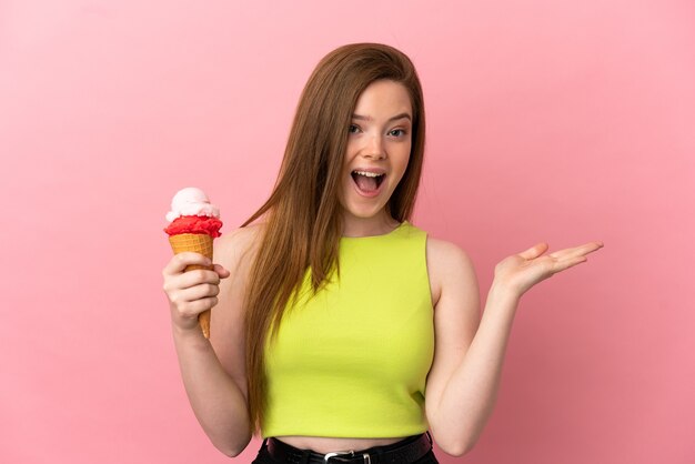 Teenager-Mädchen mit einem Kornett-Eis über isoliertem rosa Hintergrund mit schockiertem Gesichtsausdruck