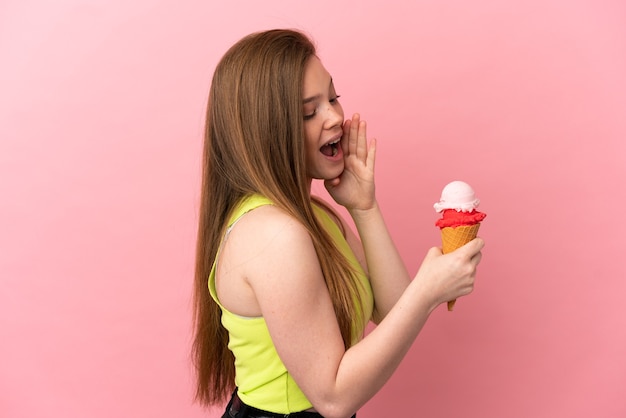 Teenager-Mädchen mit einem Kornett-Eis über isoliertem rosa Hintergrund schreien mit weit geöffnetem Mund zur Seite