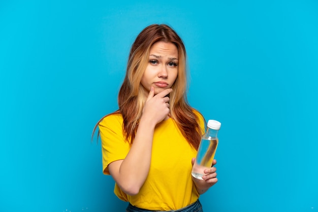 Teenager-Mädchen mit einer Flasche Wasser über isoliertem blauem Hintergrund denken