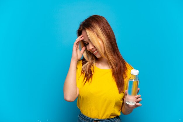 Teenager-Mädchen mit einer Flasche Wasser über isoliertem blauem Hintergrund lachen