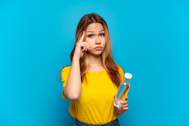 Teenager-Mädchen mit einer Flasche Wasser über lokalisiertem blauem Hintergrund, der eine Idee denkt