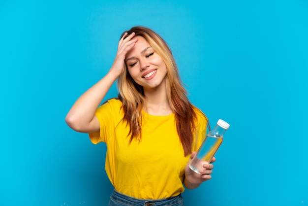 Teenager-Mädchen mit einer Flasche Wasser über lokalisiertem blauem Hintergrund, der viel lächelt