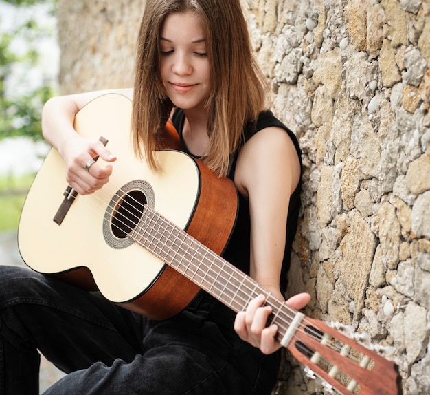 Foto teenager-mädchen mit einer gitarre gegen eine braune wand