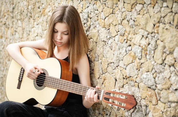 Teenager-Mädchen mit einer Gitarre gegen eine braune Wand