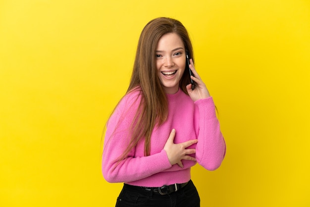 Teenager-Mädchen mit Handy über isolierten gelben Hintergrund lächelt viel