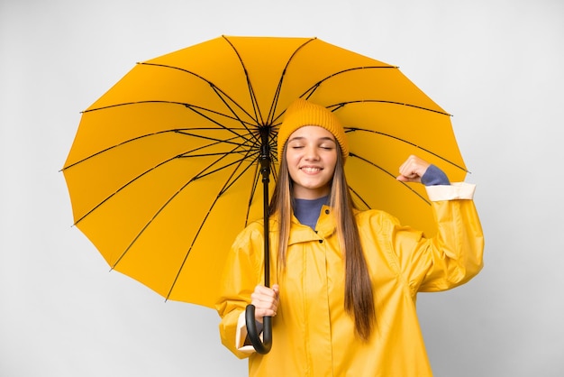 Teenager-Mädchen mit regenfestem Mantel und Regenschirm über isoliertem weißem Hintergrund, das eine starke Geste macht