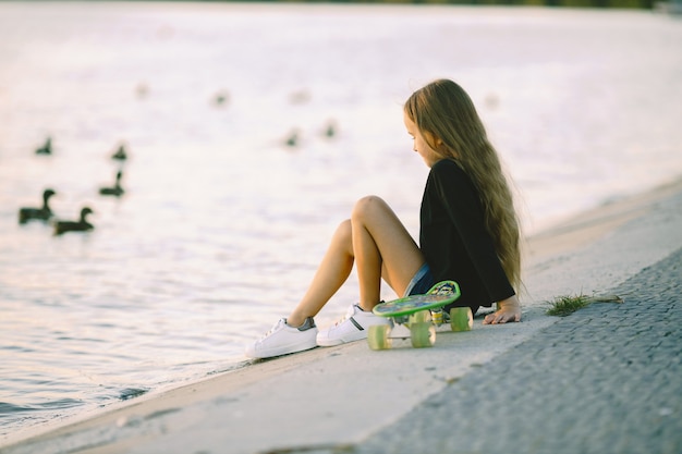 Teenager-Mädchen mit Skateboard am See sitzen