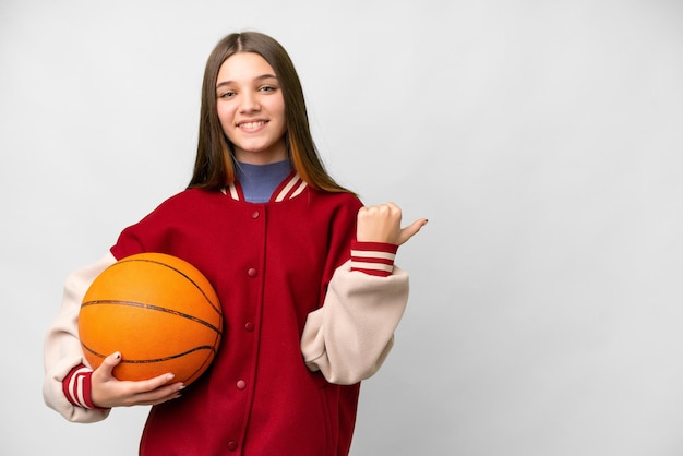 Teenager-Mädchen spielt Basketball vor isoliertem weißem Hintergrund und zeigt zur Seite, um ein Produkt zu präsentieren