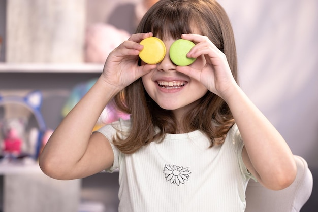 Teenager-Mädchen spielt mit Dessert-Macarons, die die Kekse wie eine Brille um die Augen halten