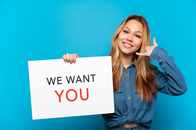 Teenager-Mädchen über isoliertem blauem Hintergrund, der We Want You Board hält und Telefongeste macht