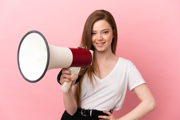 Teenager-Mädchen über isoliertem rosa Hintergrund, der ein Megaphon hält und viel lächelt