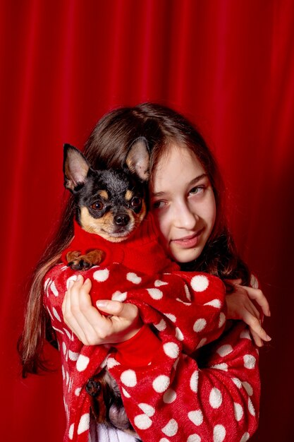 Teenager-Mädchen und ein Chihuahua gekleidet in einem roten Pullover für Hunde zu Hause vor einem roten Hintergrund.