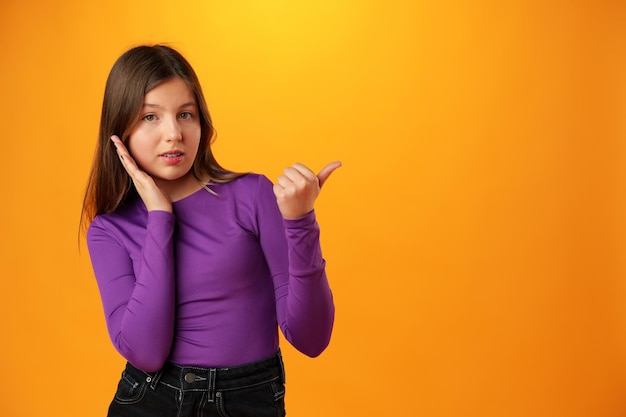 Teenager-Mädchen vor gelbem Hintergrund zeigt mit dem Finger auf den Kopierraum