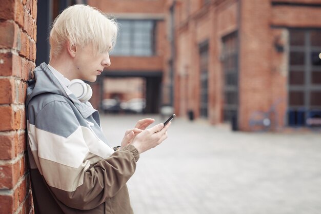 Teenager mit blonden Haaren, die an der Wand des Backsteingebäudes stehen und SMS schreiben