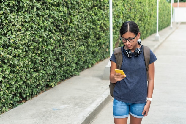 Teenager mit drahtlosem Headset, das Smartphone in einem Park überprüft.