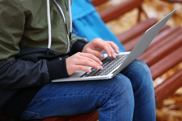 Teenager mit Laptop, der auf Bank im Herbstpark, nah oben sitzt